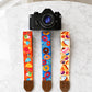 Camera with colorful camera straps featuring various designs on a marble surface.