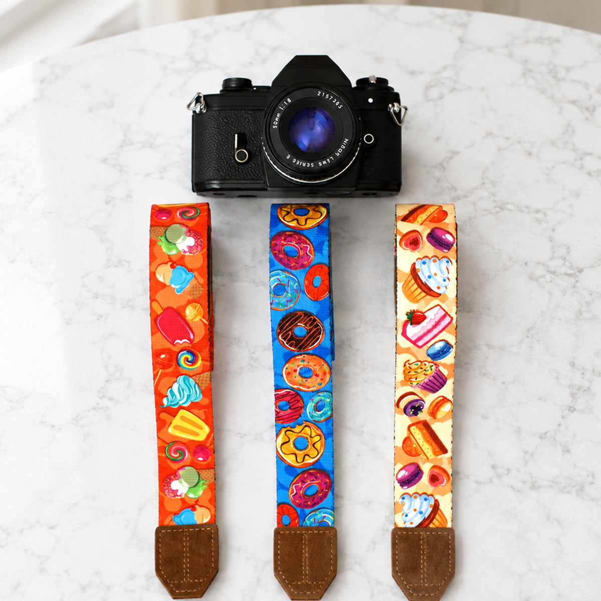 Camera with colorful camera straps featuring various designs on a marble surface.