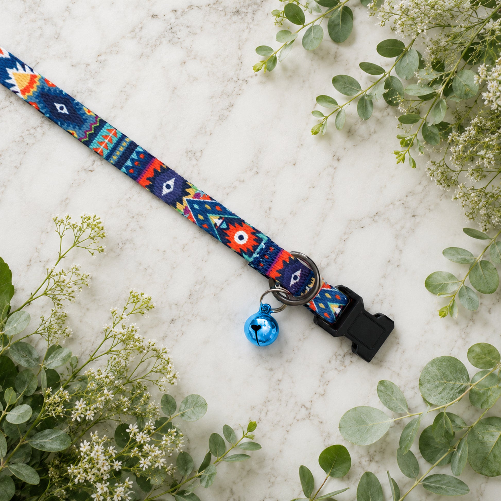 Colorful dog collar with a bell on a light background with greenery