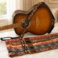 Acoustic guitar with a patterned strap on a marble surface