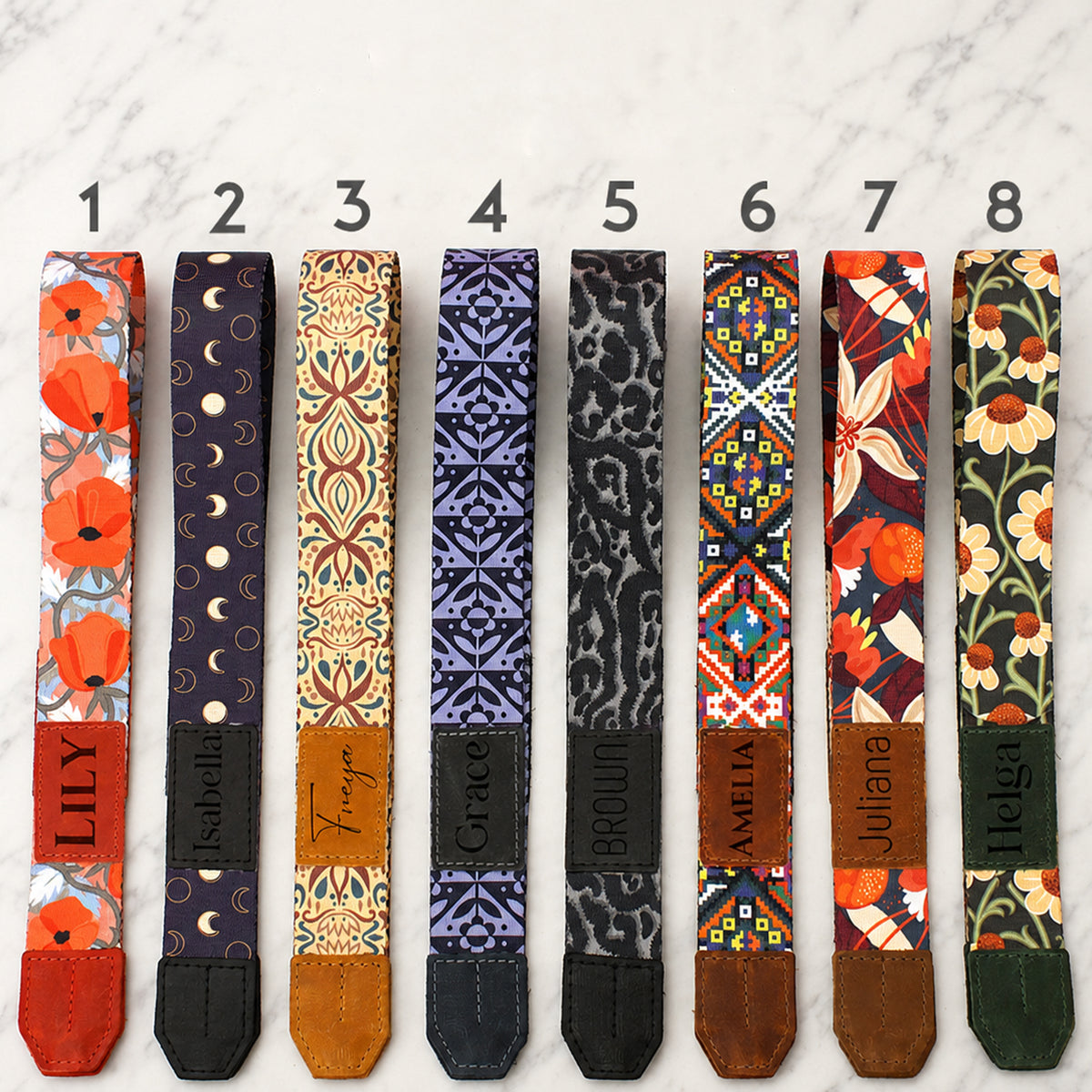 Eight colorful guitar straps with different patterns and names on a light gray background
