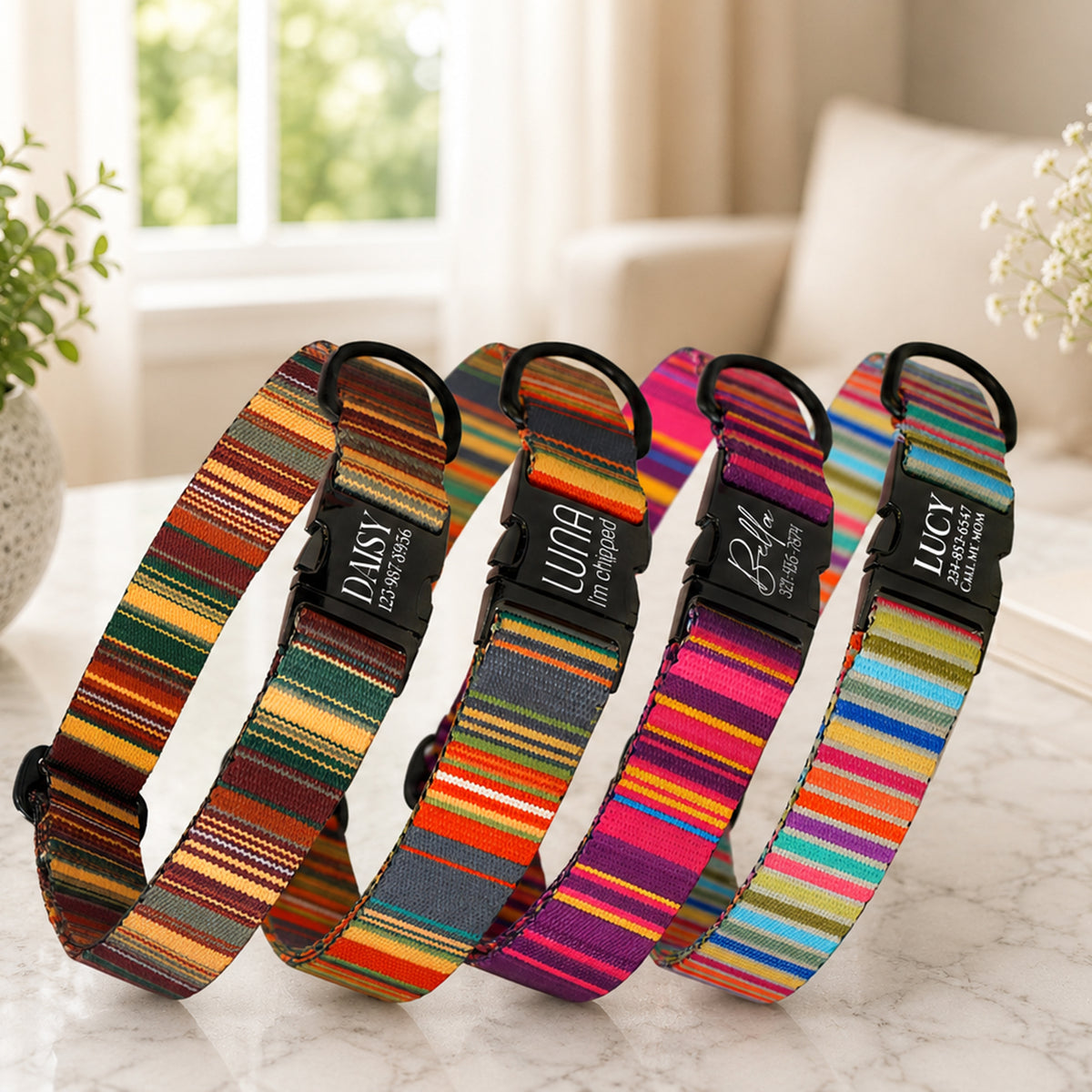 Four colorful striped dog collars with names on black tags on a marble surface.
