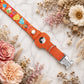 Orange dog collar with colorful designs and a silver tag on a marble surface with flowers.
