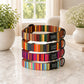 Stack of colorful striped dog collars on a marble surface with plants in the background