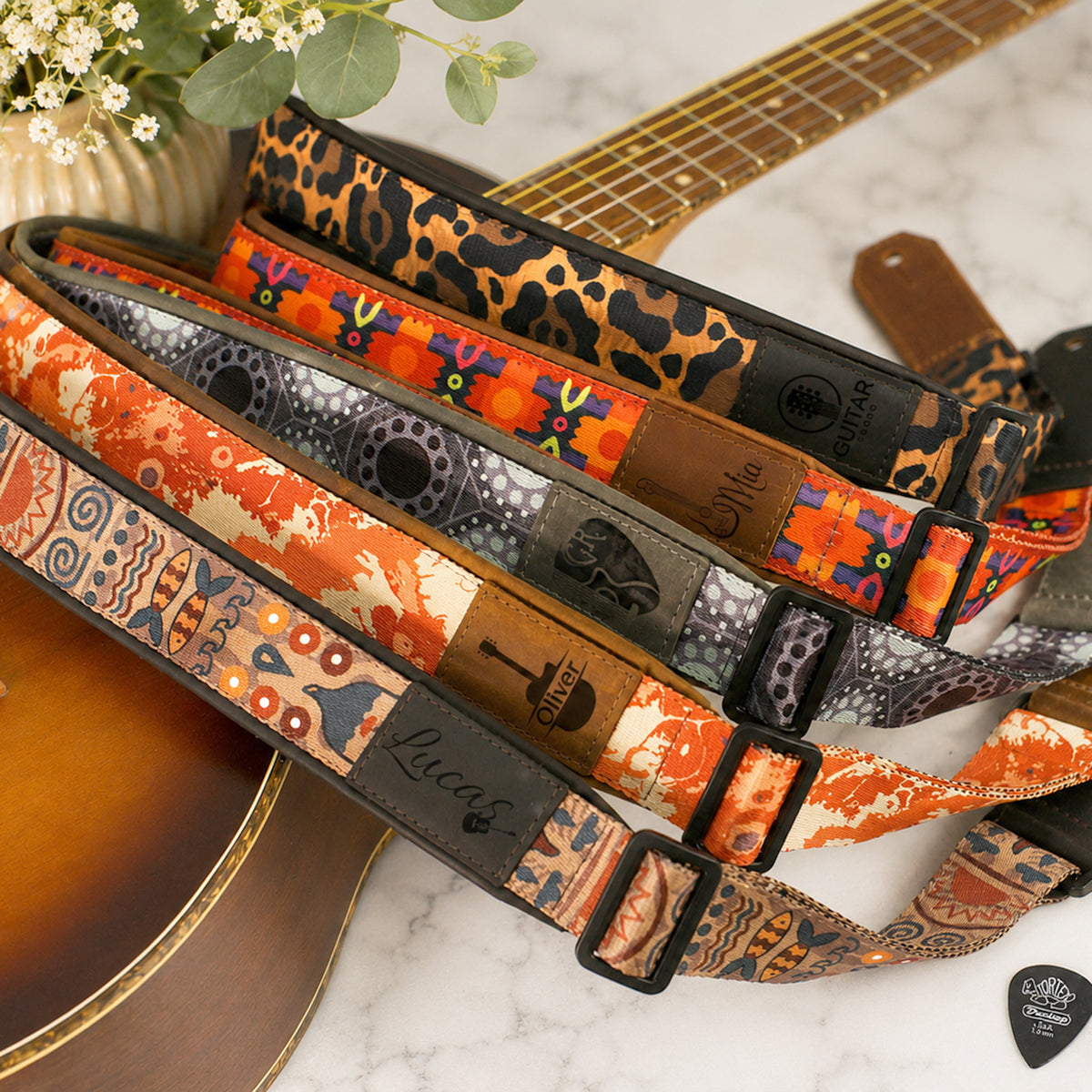 Collection of colorful guitar straps with 'Lucas' branding on a marble surface.