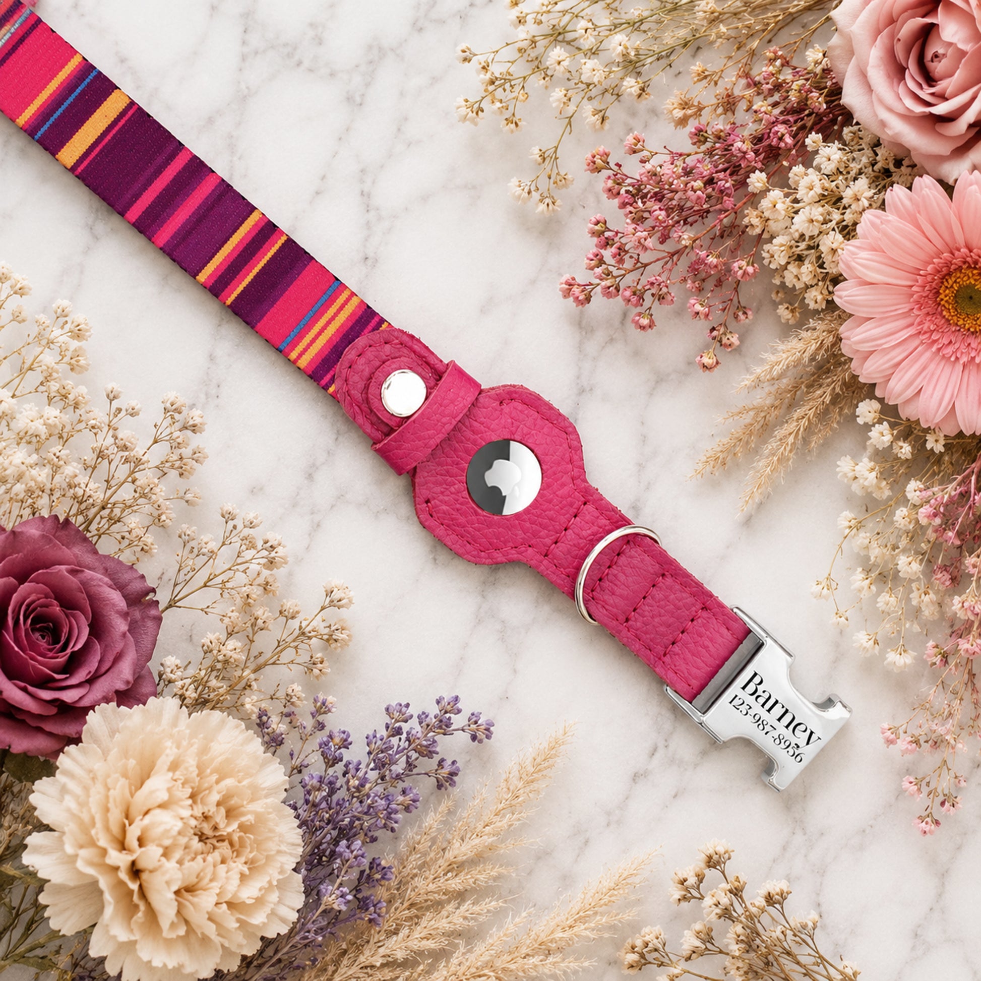 Pink dog collar with colorful stripes on a marble surface surrounded by flowers