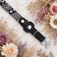 Black dog collar with silver buckle on a marble surface surrounded by flowers