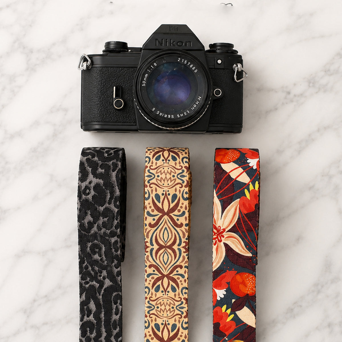 Black Nikon camera with three patterned camera straps on a marble surface