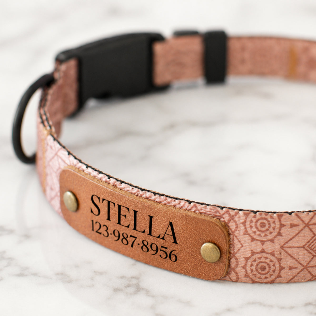 Dog collar with a patterned band and leather nameplate on a marble surface