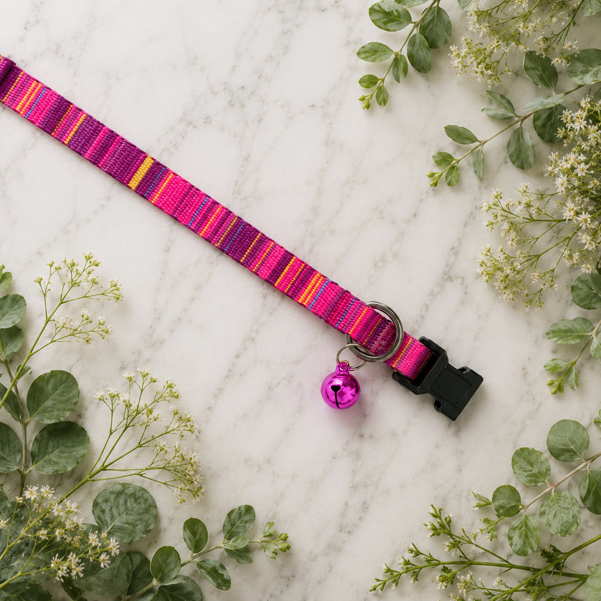 Pink striped dog collar with a bell on a marble surface with greenery