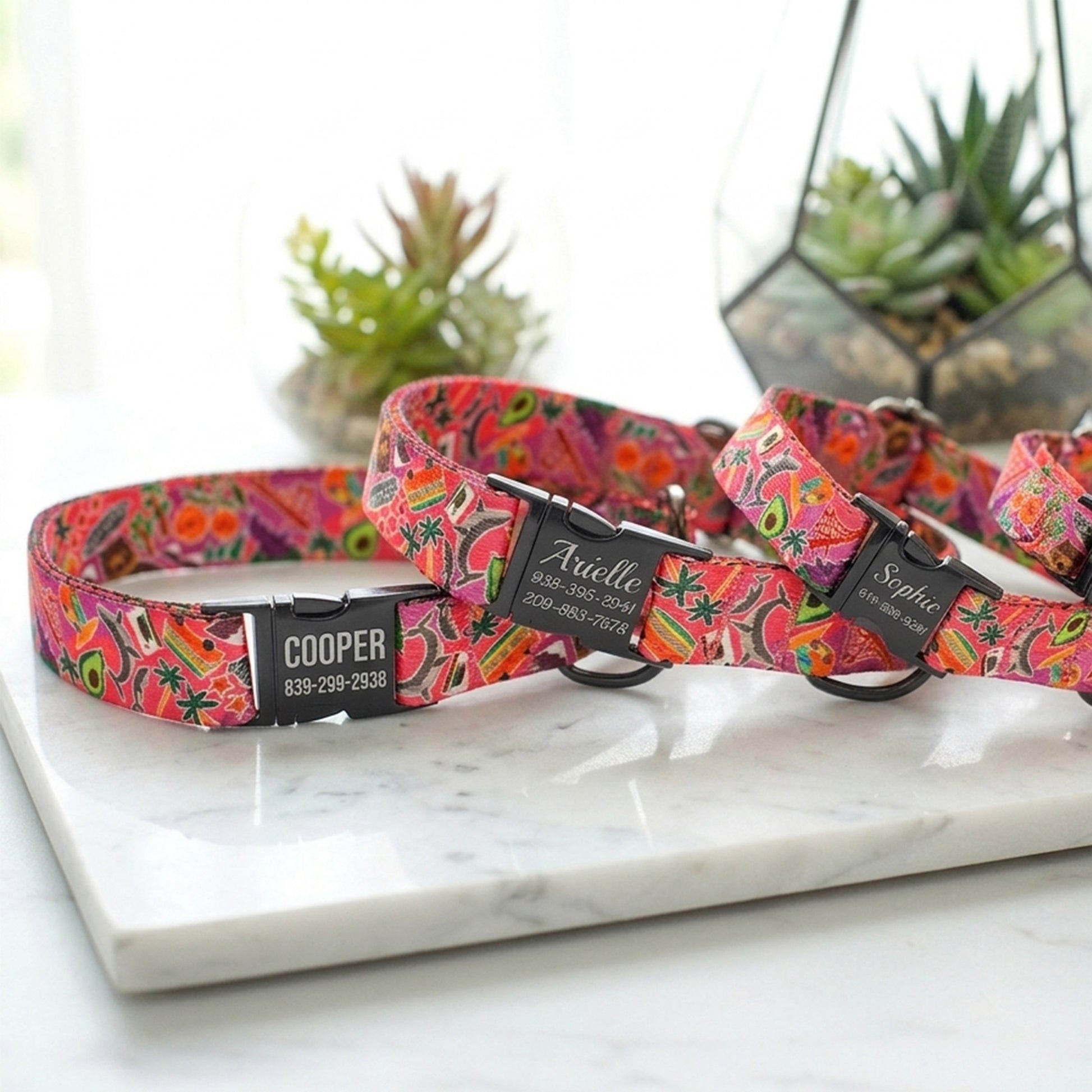 Colorful floral-patterned dog collars with engraved names on a marble surface.
