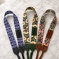 Three colorful camera straps with floral and geometric patterns on a marble surface.