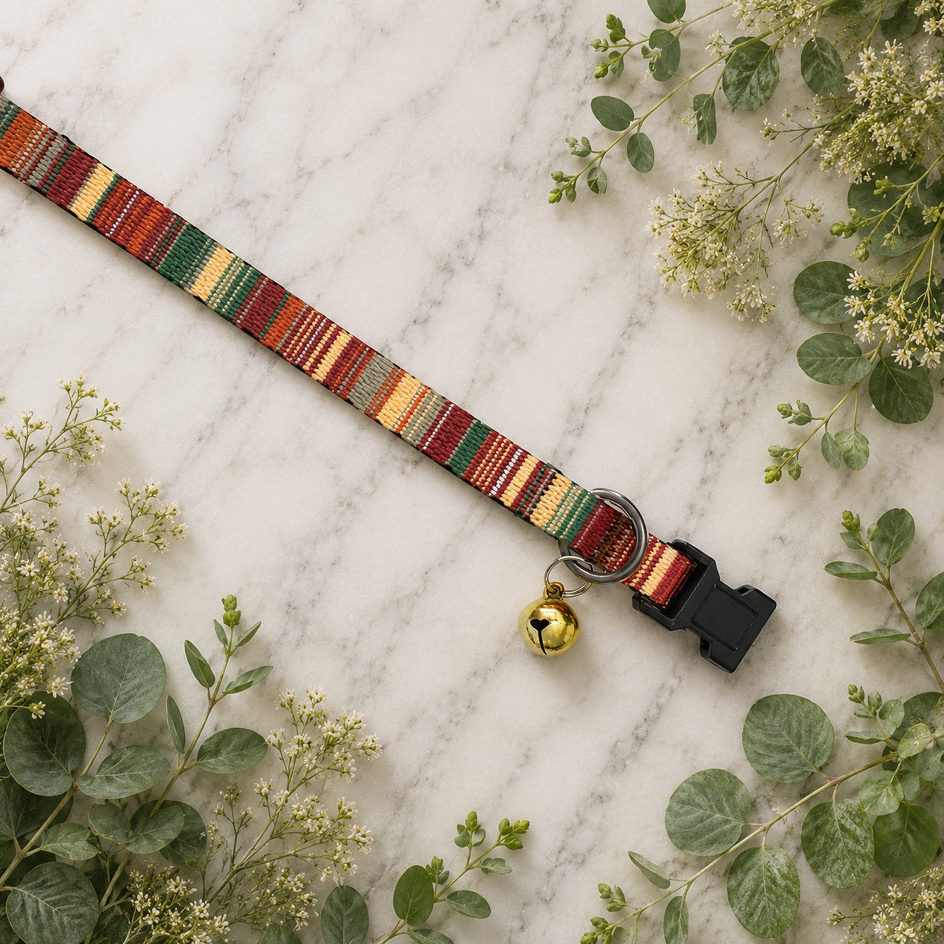 Colorful striped dog collar with a bell on a marble surface with greenery