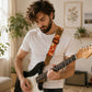 Man playing an electric guitar in a room with plants and a couch.
