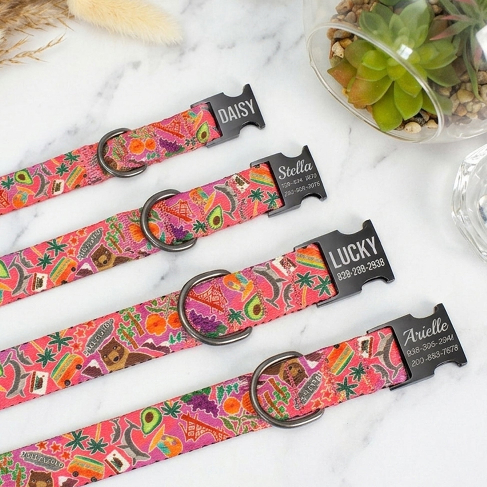 Colorful patterned pet collars with engraved names on a marble surface.