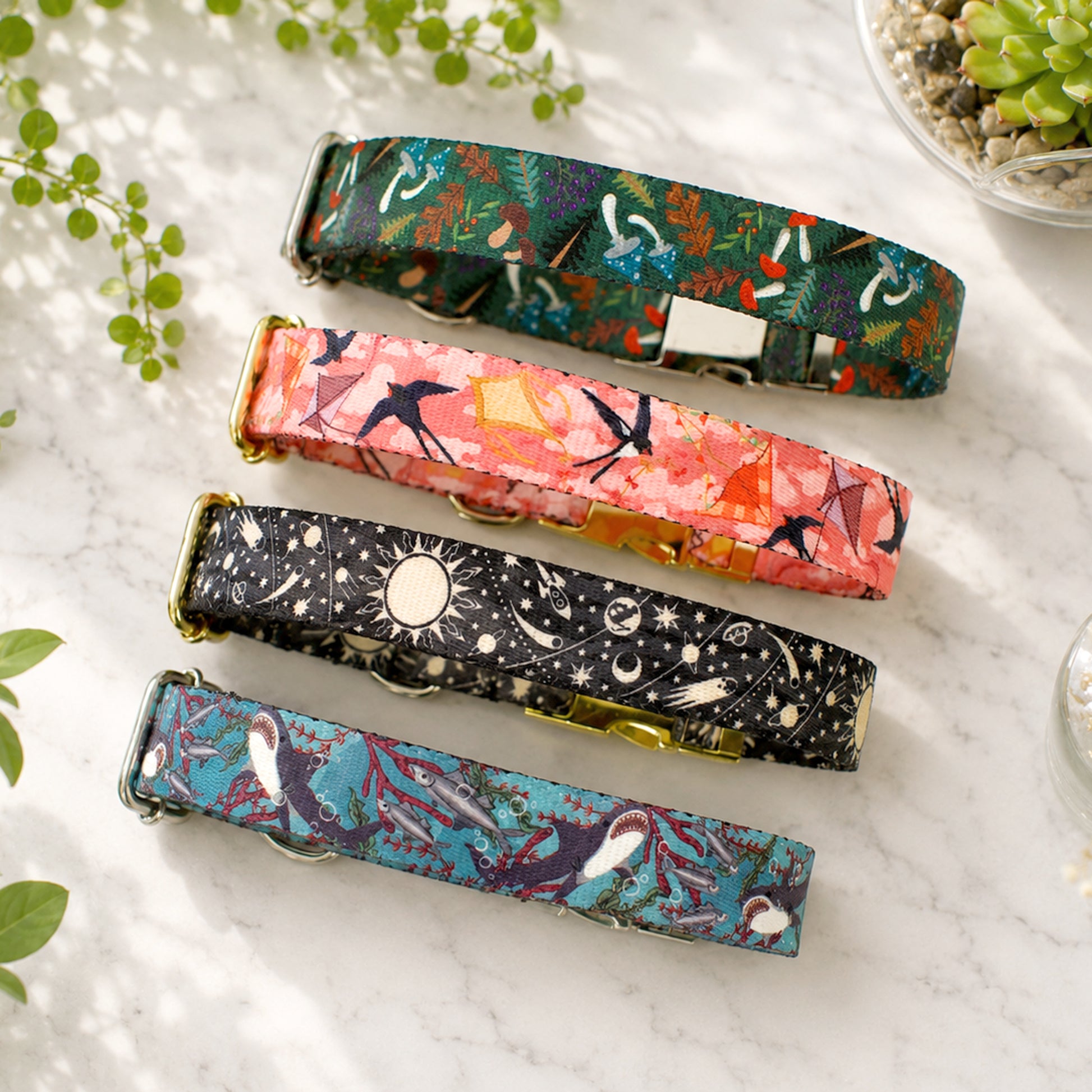 Four colorful dog collars with different patterns on a marble surface.