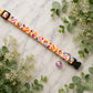 Colorful dog collar with floral pattern and bell on marble surface with greenery