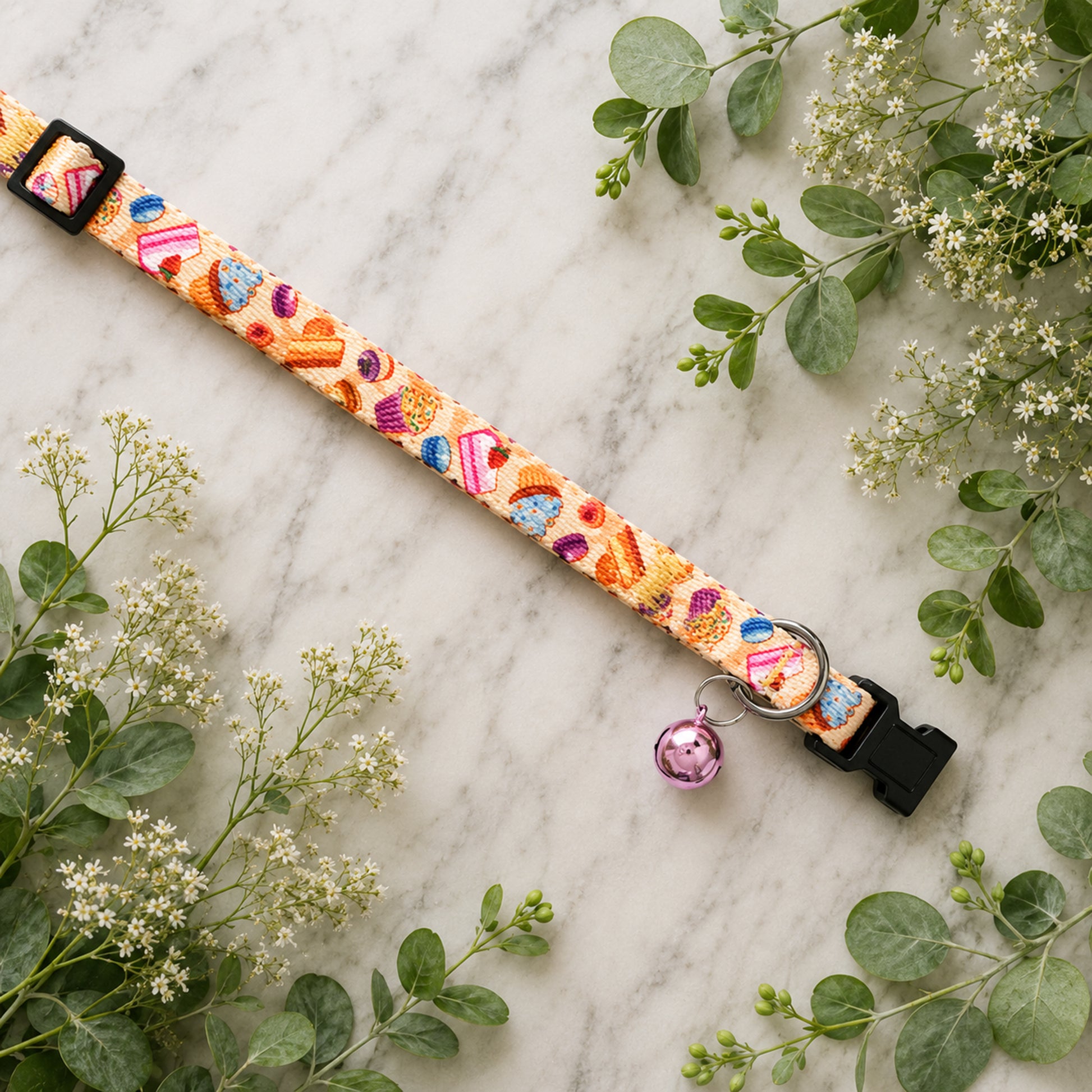 Colorful dog collar with floral pattern and bell on marble surface with greenery