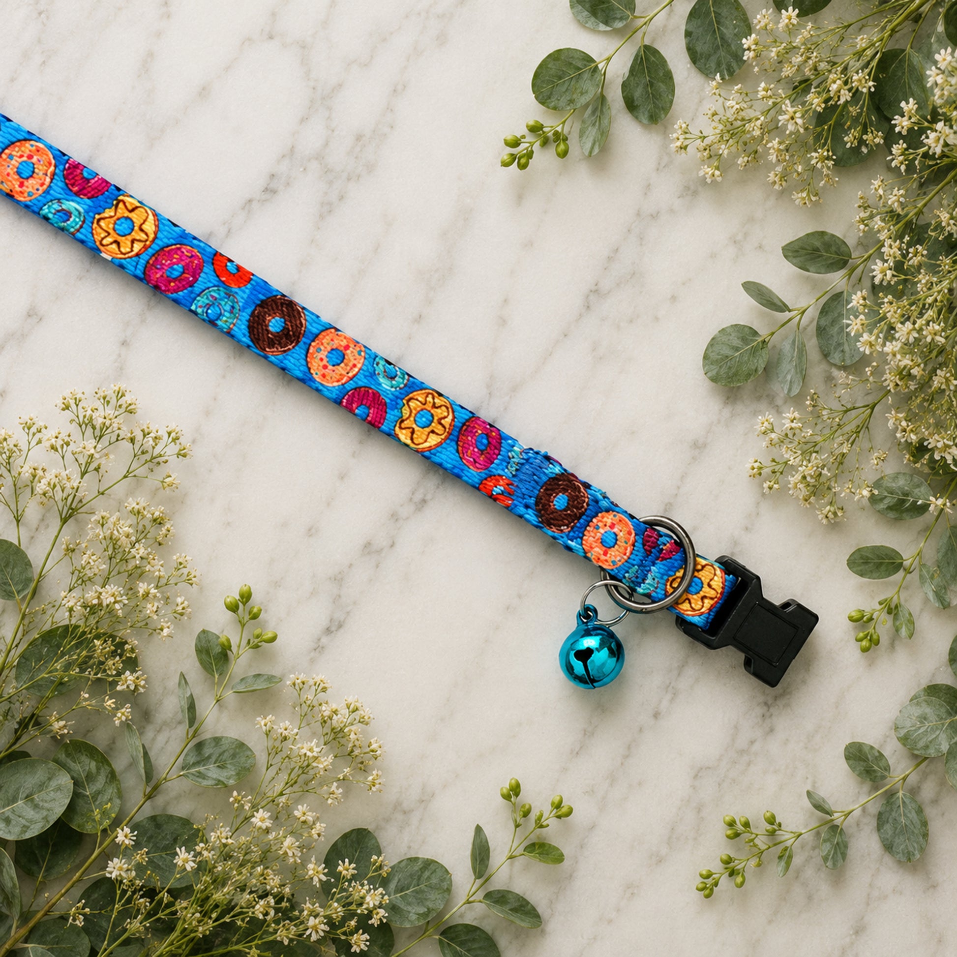 Colorful donut-patterned dog collar with a bell on a marble surface with greenery.