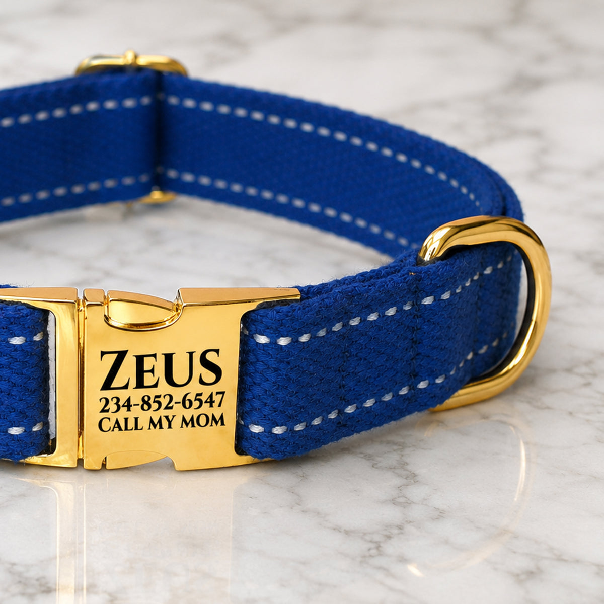 Blue dog collar with gold buckle and engraved tag on a marble surface