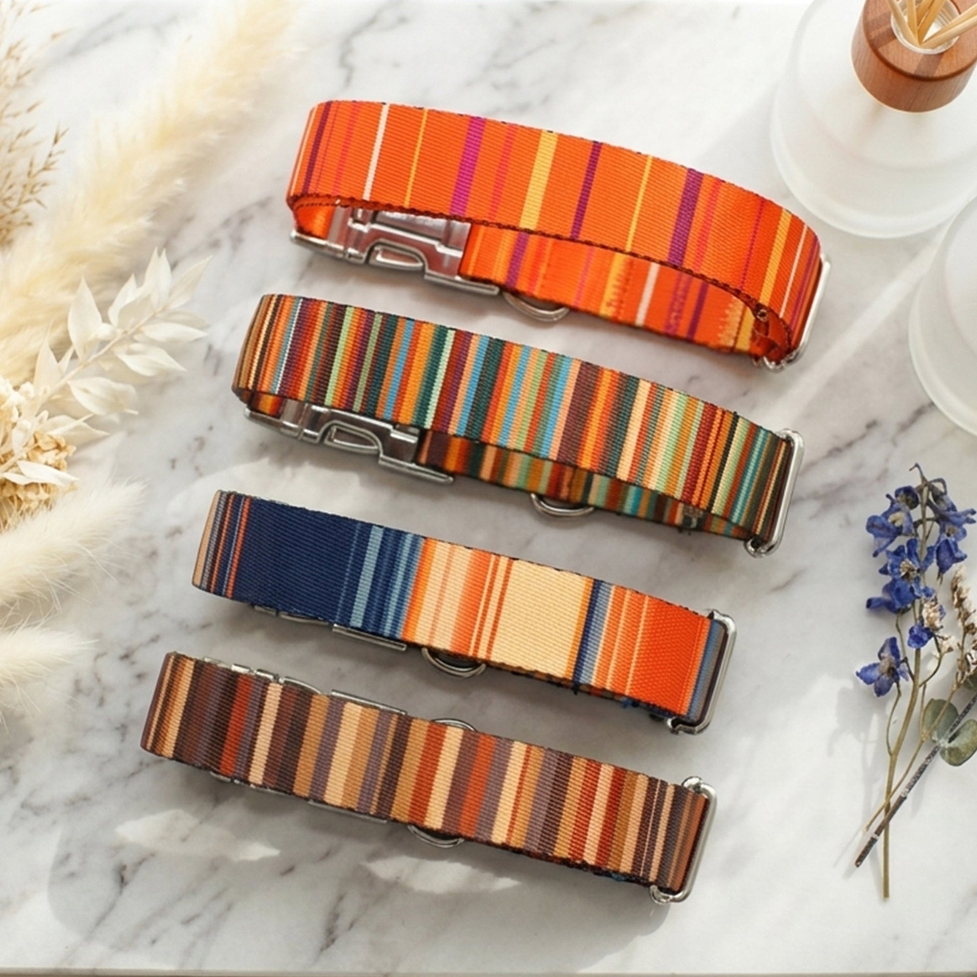 Four striped dog collars in orange, multicolor, blue, and brown on a marble surface.